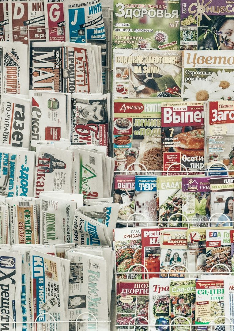 Link zum Pressespiegel Verschiedene Zeitungen und Magazine übereinander gestapelt, bunt bedruckte Seiten.