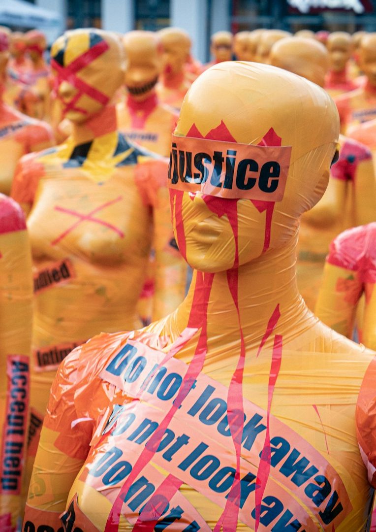 Link zu Gerichtsbeschlüssen Gelbe Mannequins mit roten und schwarzen Schriftzügen für Gerechtigkeit und Protest.